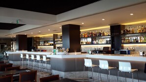 A bar area with a counter, bar stools, and a variety of bottles and glasses on shelves.