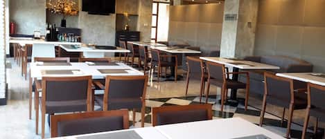 A modern restaurant with multiple tables and chairs, a TV mounted on the wall, and a decorative vase with flowers.
