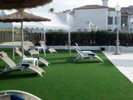 Terraza en la azotea con césped artificial, sillones de descanso y una carpa blanca.