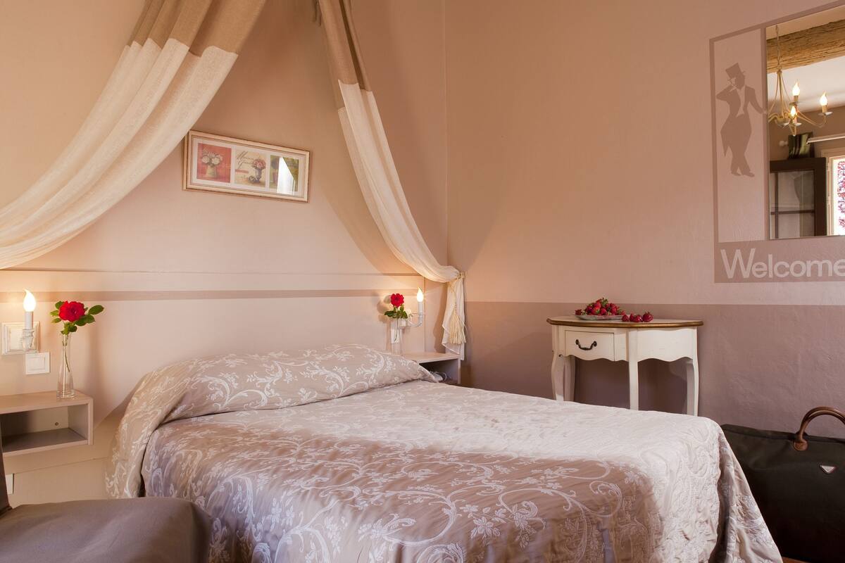 Un dormitorio con cama con dosel, mesitas de noche con lámparas, un espejo y un cartel de bienvenida.