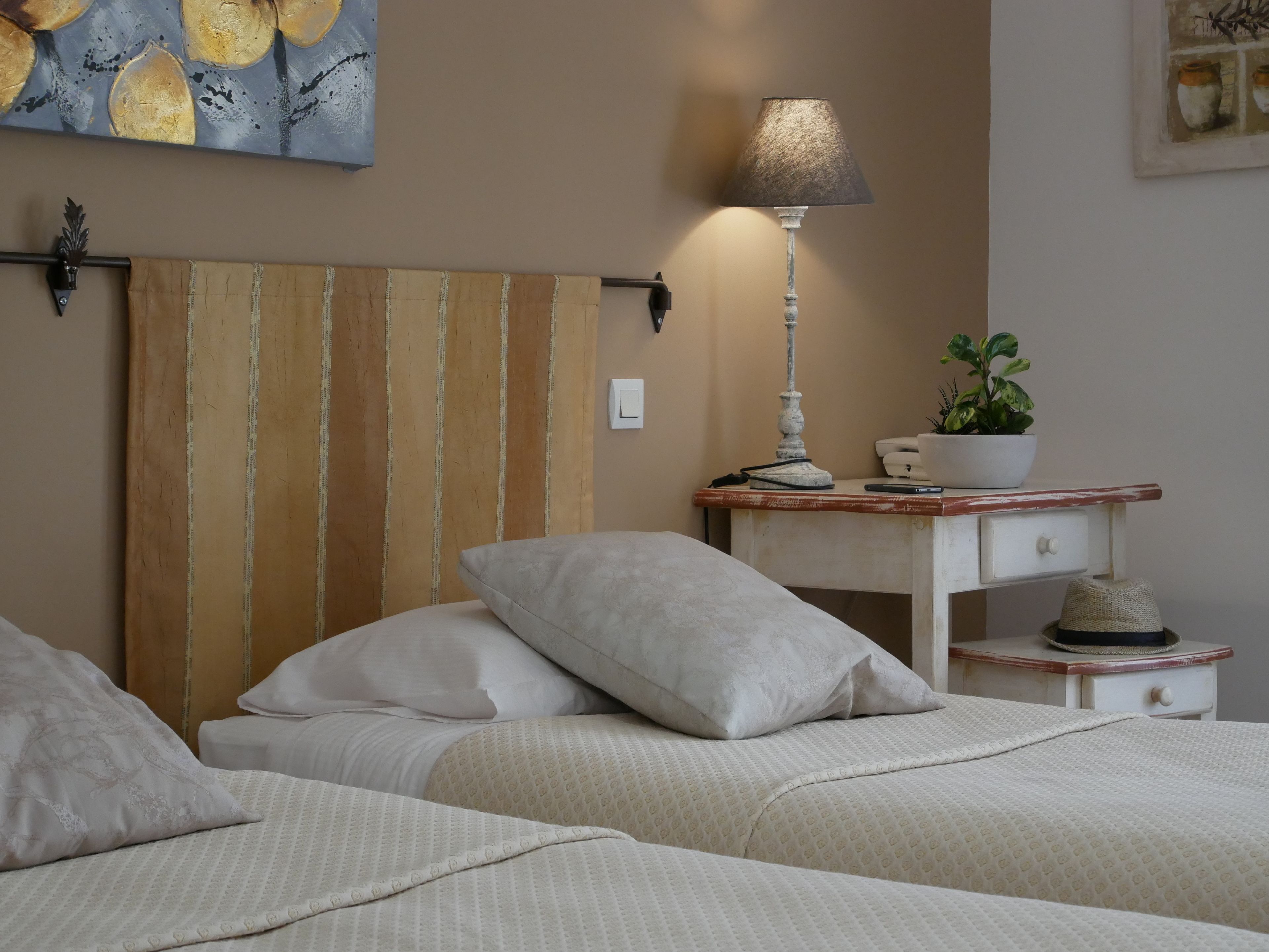 Una camera da letto con una testiera a righe, un comodino con una lampada, una pianta in vaso e un piccolo oggetto decorativo.