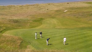 A golf course with a view of the sea and a distant hill.