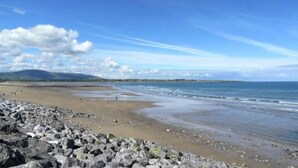A beach with rocky foreground, calm water, and distant hills.