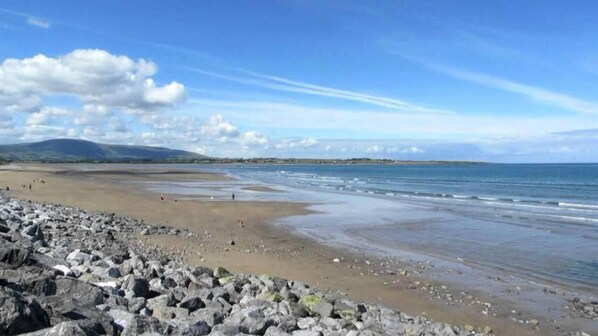 A beach with rocky foreground, calm water, and distant hills.