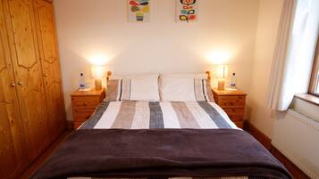 A bedroom with a bed, wooden wardrobe, bedside tables with lamps, and wall art.