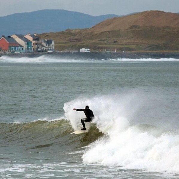 A person surfing on a wave with buildings in the background. - Old Fort Lodge (Sligo)
