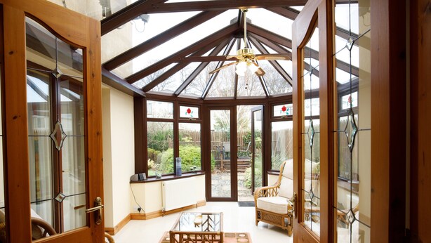 A conservatory with a glass ceiling, wooden beams, and a ceiling fan.