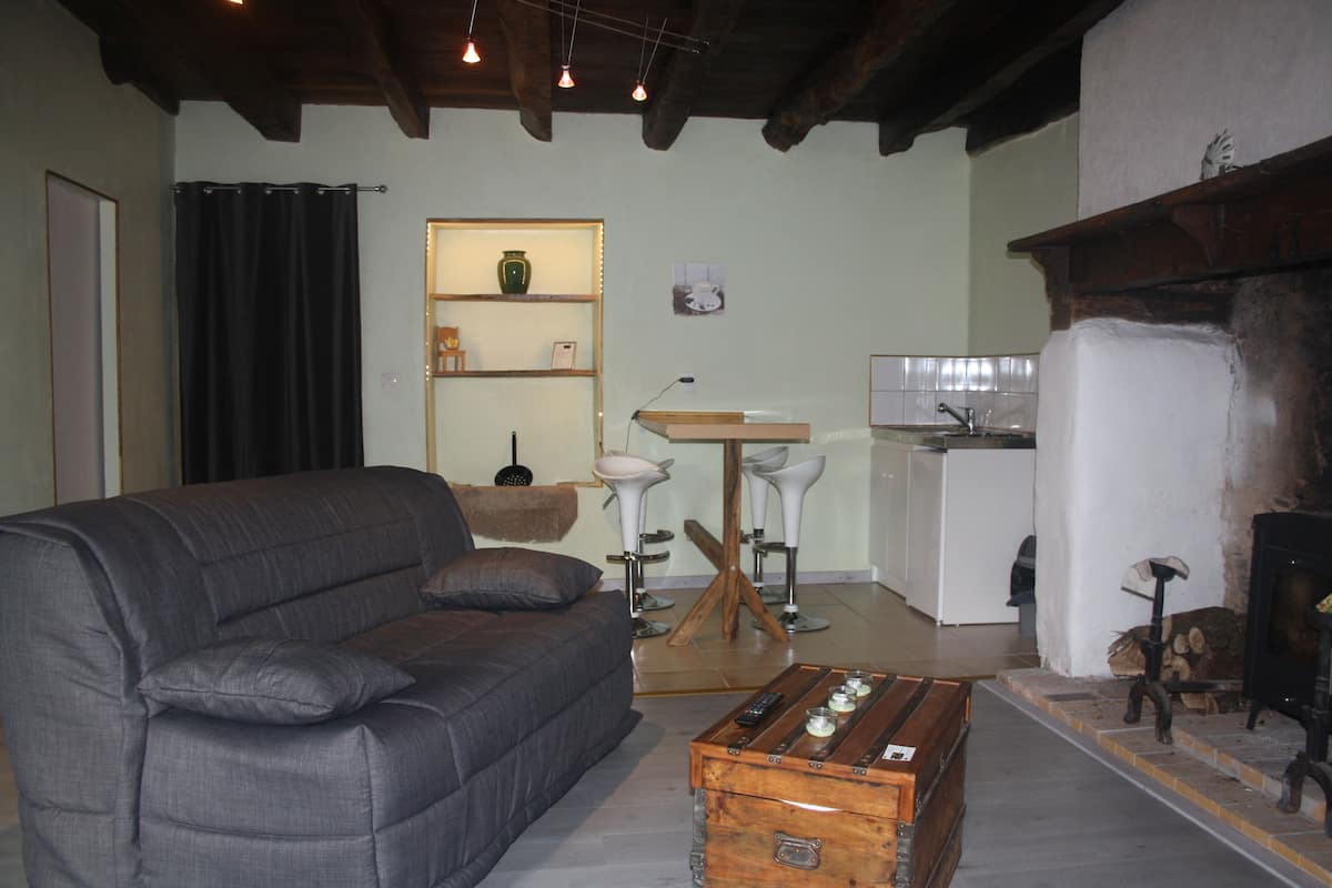 Una sala de estar con sofá, una mesita de centro, chimenea y una zona de cocina al fondo.
