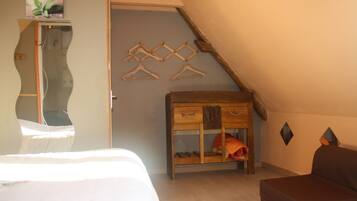 Une chambre avec un plafond en pente, une commode en bois, un lit et un porte-manteau fixé au mur.