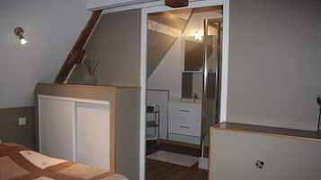 A bedroom with a bed, a dresser, a mirror, and a small bathroom with a sink and towel rack.