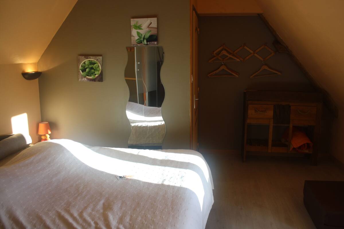 Un dormitorio con cama, un espejo montado en la pared, una planta colgante y un aparador de madera.
