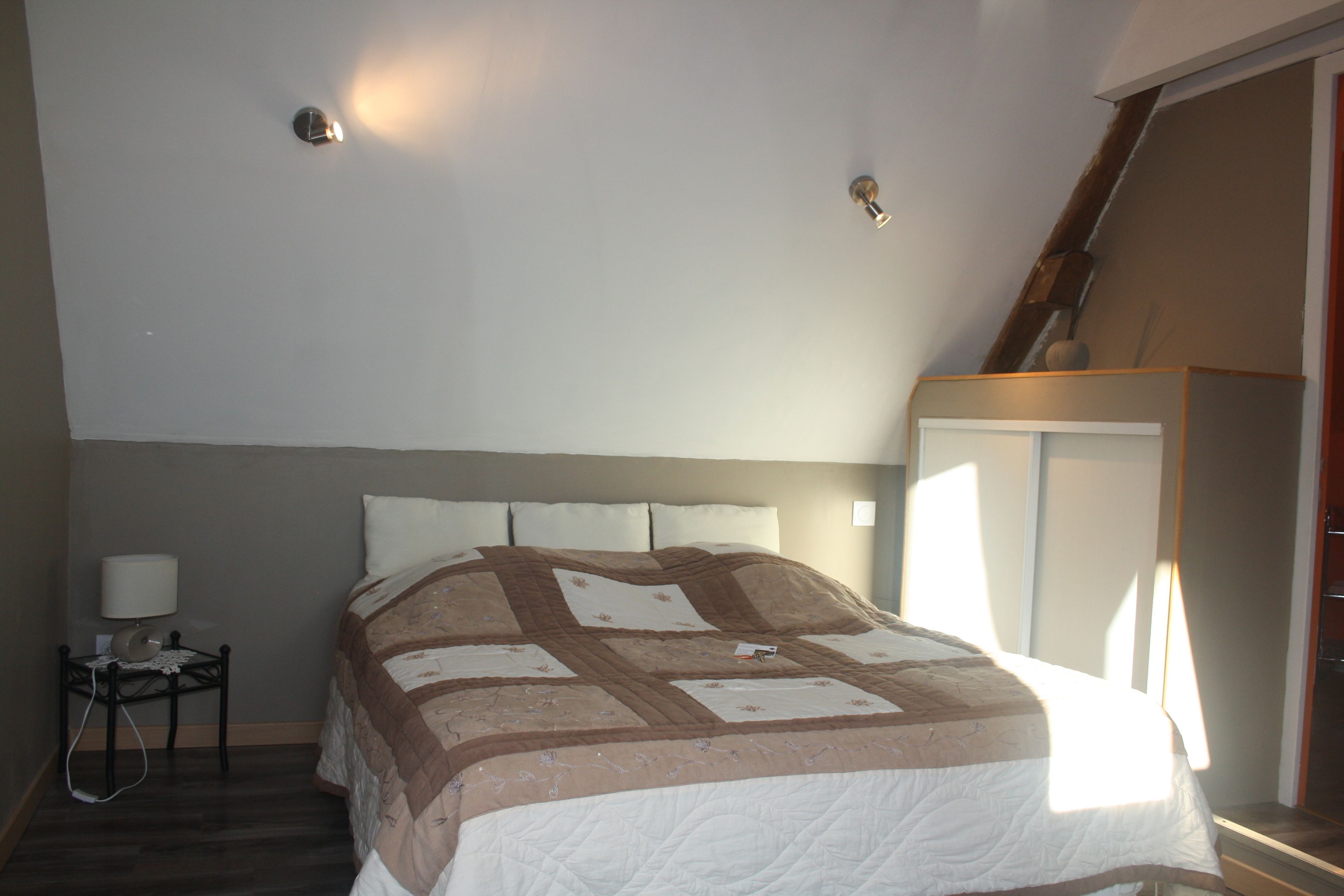 Une chambre à coucher comprenant un lit, une table de chevet, une lampe et une fenêtre donnant sur un escalier.