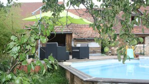 Una piscina con muelle de madera, mobiliario exterior y una sombrilla verde.