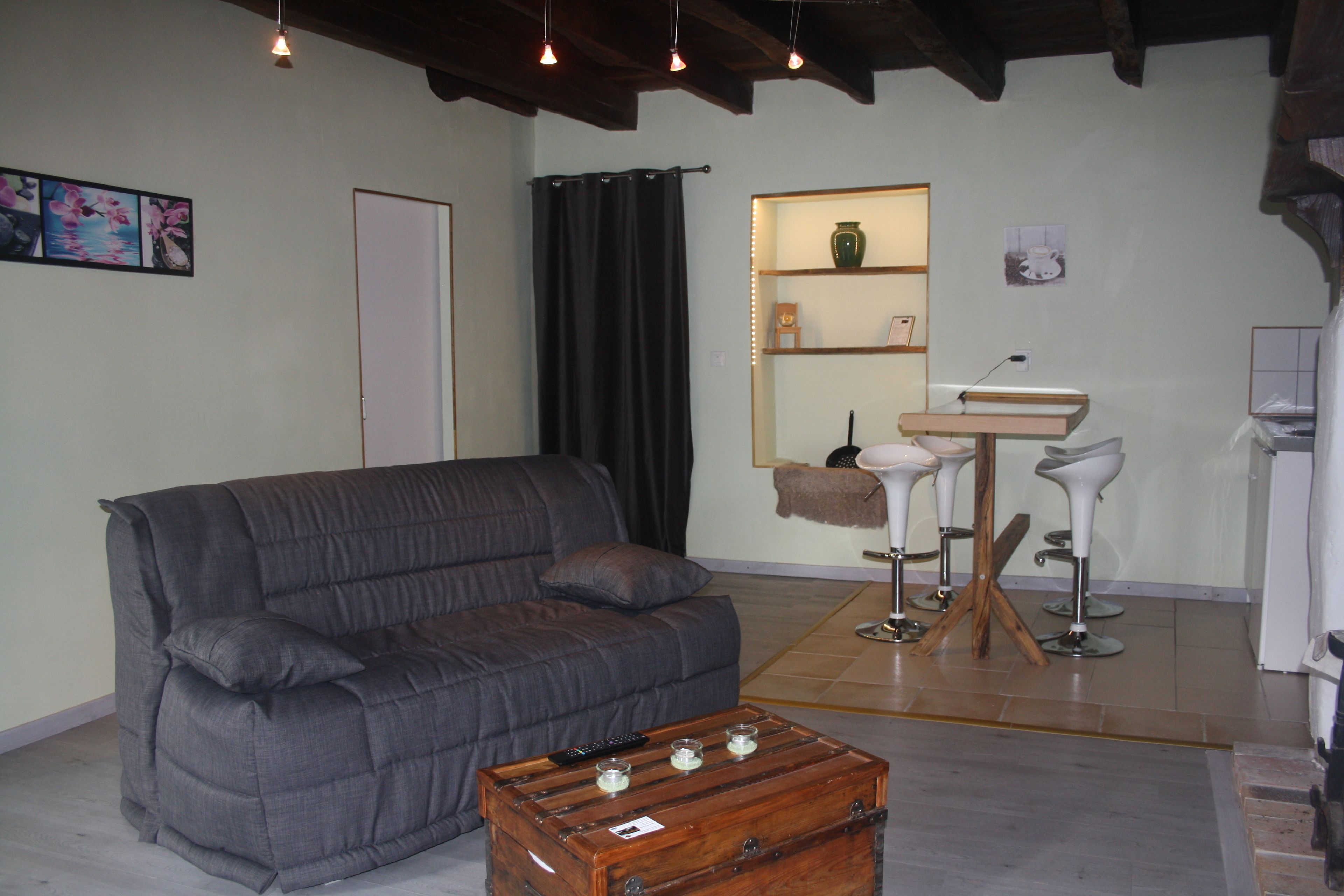Uma sala de estar com um sofá cinzento, um baú de madeira e uma pequena mesa com bancos.