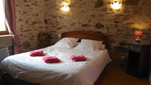 Una cama con sábanas blancas y almohadas rosas, cabecera de madera y paredes de piedra.