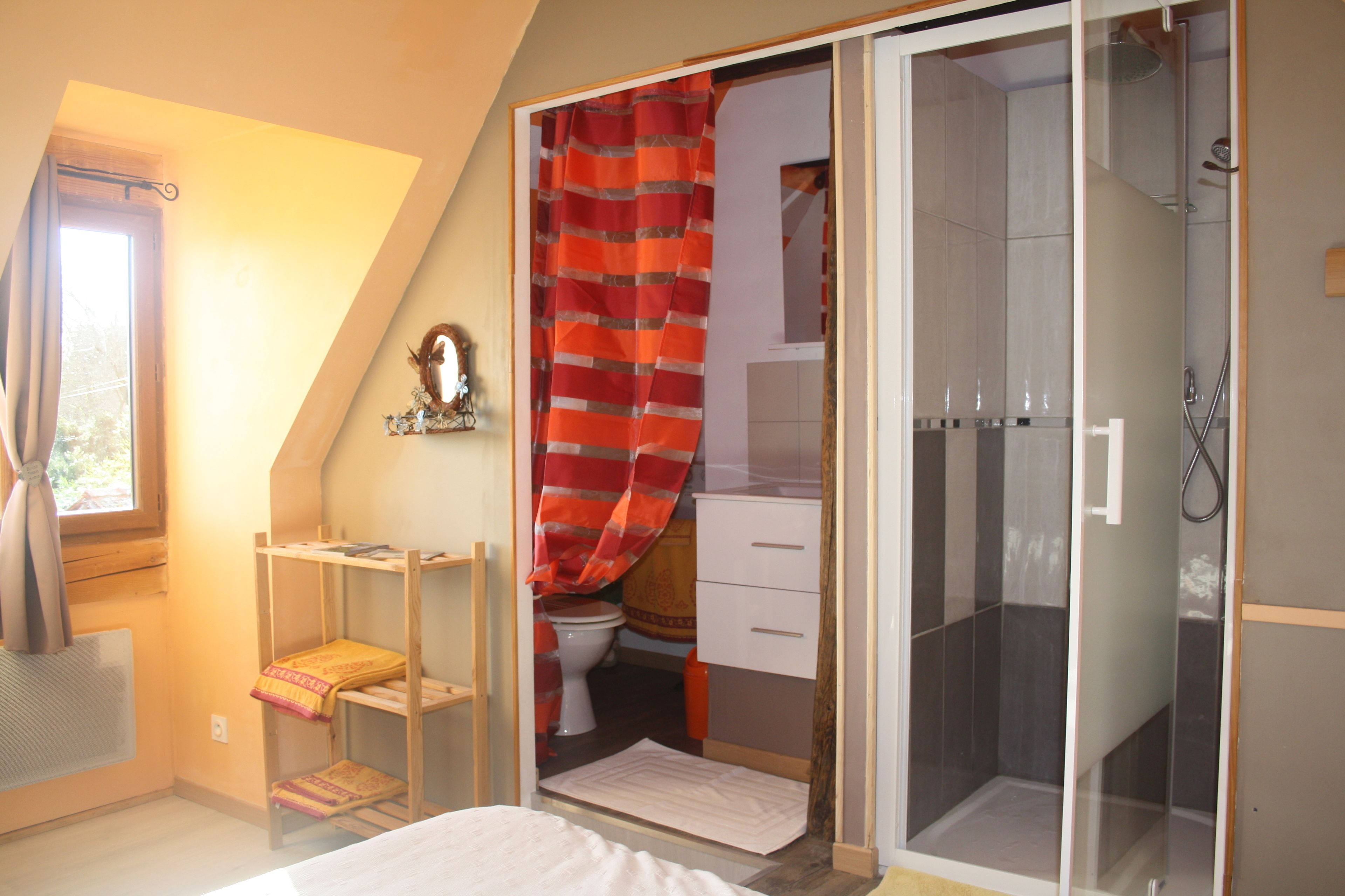 A bedroom with a bunk bed, a shower with a glass door, a toilet, and a small window with curtains.