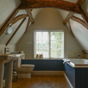 Bagno con vasca, servizi igienici e lavandino, con travi in legno e finestra dotata di persiane.