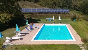 A rectangular swimming pool with a tiled deck, surrounded by grass and trees. - Agriturismo Il Corniolo (Castiglione di Garfagnana)