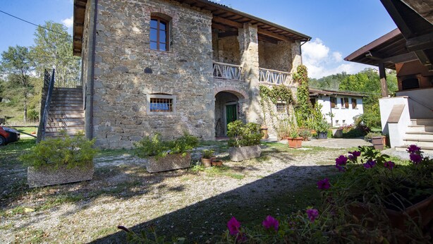 A stone building with a balcony, a green door, and potted plants. - Agriturismo Il Corniolo (Castiglione di Garfagnana)