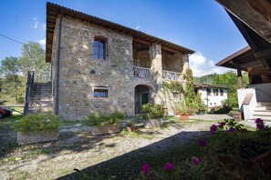 A stone building with a balcony, a green door, and potted plants. - Agriturismo Il Corniolo (Castiglione di Garfagnana)