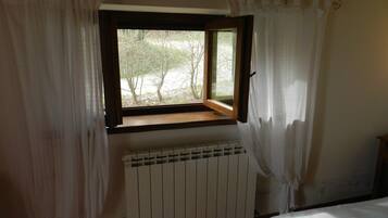 A room with a window, white curtains, a radiator, and a bed.