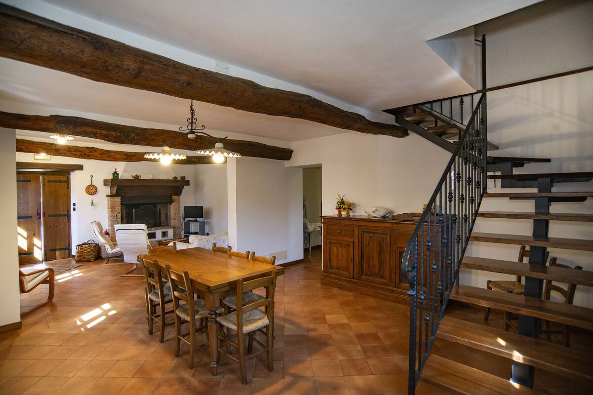 A spacious dining area with a wooden table and chairs, a fireplace, and a staircase with a metal railing.