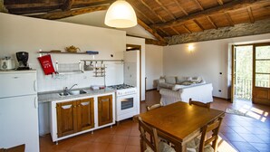 A kitchen with wooden cabinets, a stove, and a dining area with a wooden table and chairs. - Agriturismo Il Corniolo (Castiglione di Garfagnana)