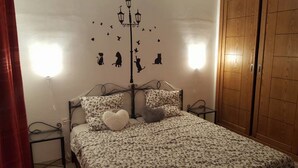 A bedroom with a bed, patterned bedding, a heart-shaped pillow, a nightstand, a lamp, and a wardrobe. - Maryouma Appart (Nabeul)