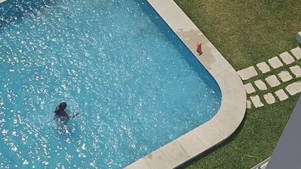 A swimming pool with a person swimming, surrounded by a grassy area and a paved walkway. - Maryouma Appart (Nabeul)