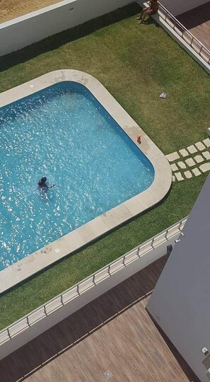 Une piscine où une personne nage, entourée d’une zone herbeuse et d’un chemin pavé.