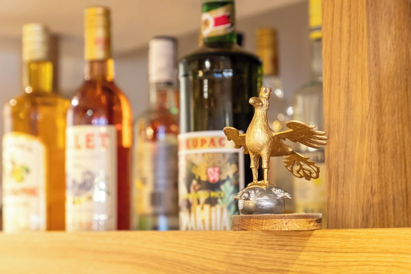 Una repisa con varias botellas de licor y una figurita decorativa de gallo dorado.