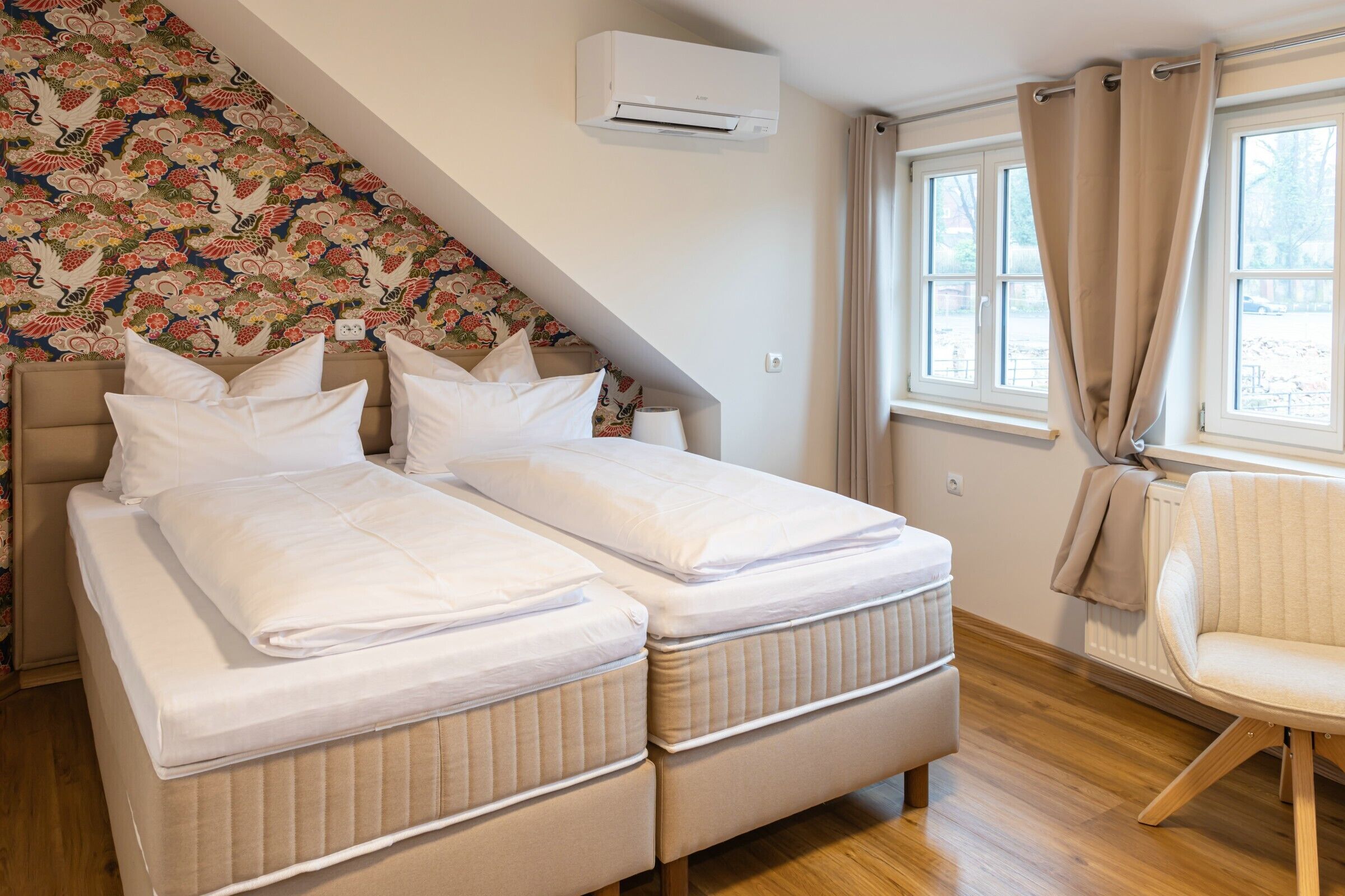 Ein Schlafzimmer mit zwei Betten, einem Fenster mit Vorhängen, einer Klimaanlage und einer Wand mit Muster.