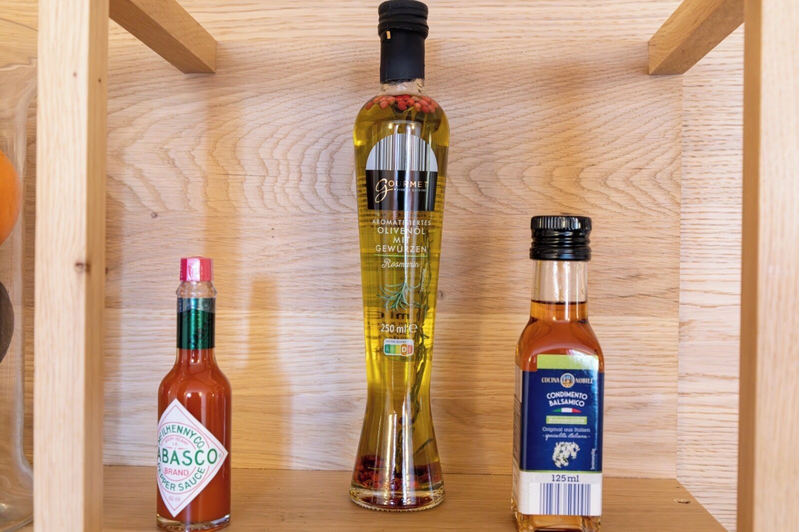 Tres botellas de salsas y aderezos sobre una repisa de madera.