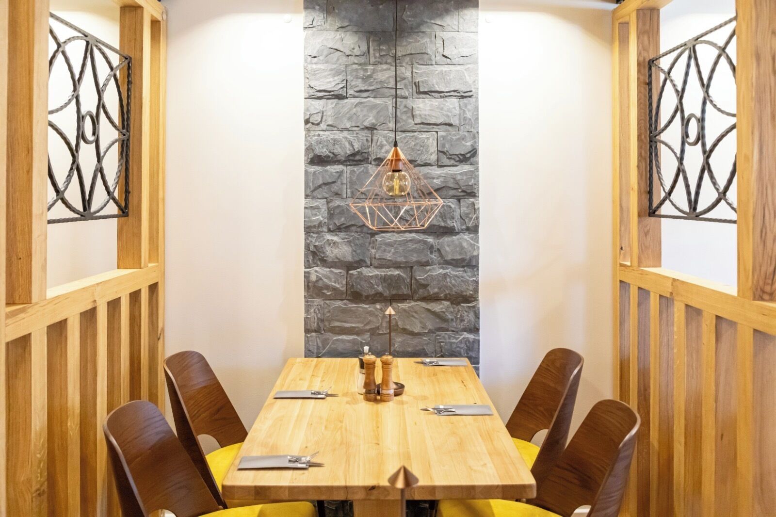 Un comedor con una mesa de madera, cuatro sillas, una pared de piedra y detalles decorativos de metal.