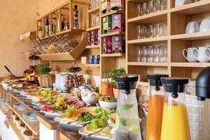 Un bufé con diversos alimentos, incluyendo carnes, quesos y frutas. También hay varias botellas de bebidas y una variedad de copas.