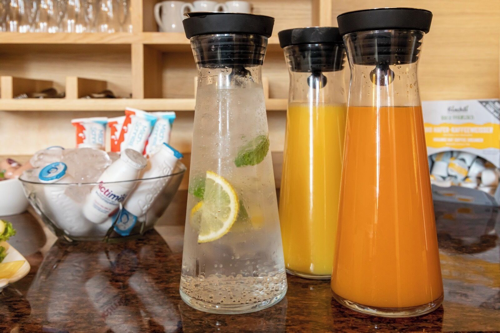 Three glass bottles with different colored liquids, a bowl of ice, and some packets on a countertop.