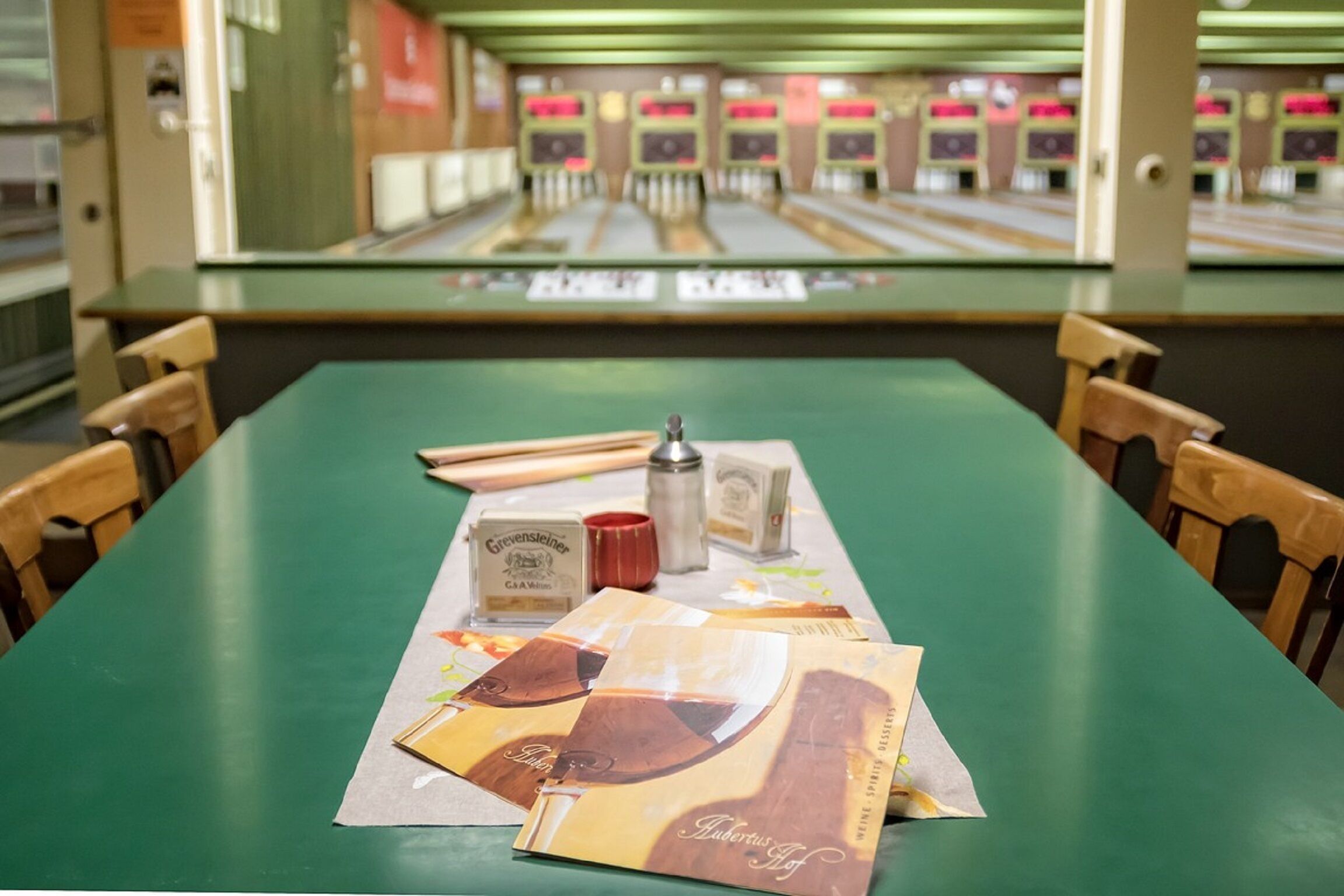 A bowling alley with a green table in the foreground and bowling lanes in the background.