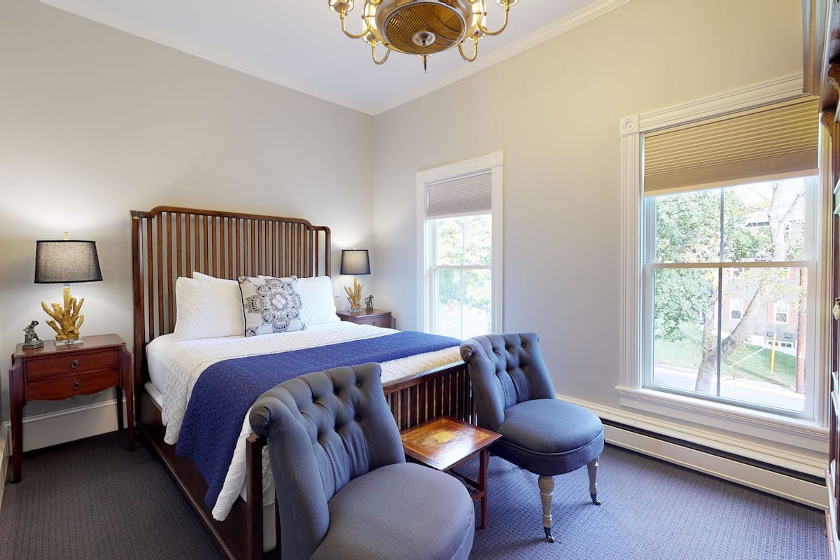Une chambre à coucher avec un grand lit, deux tables de chevet, une chaise et une fenêtre avec des stores.