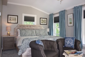 Une chambre avec un grand lit, une table de chevet, une chaise et une fenêtre avec des rideaux.