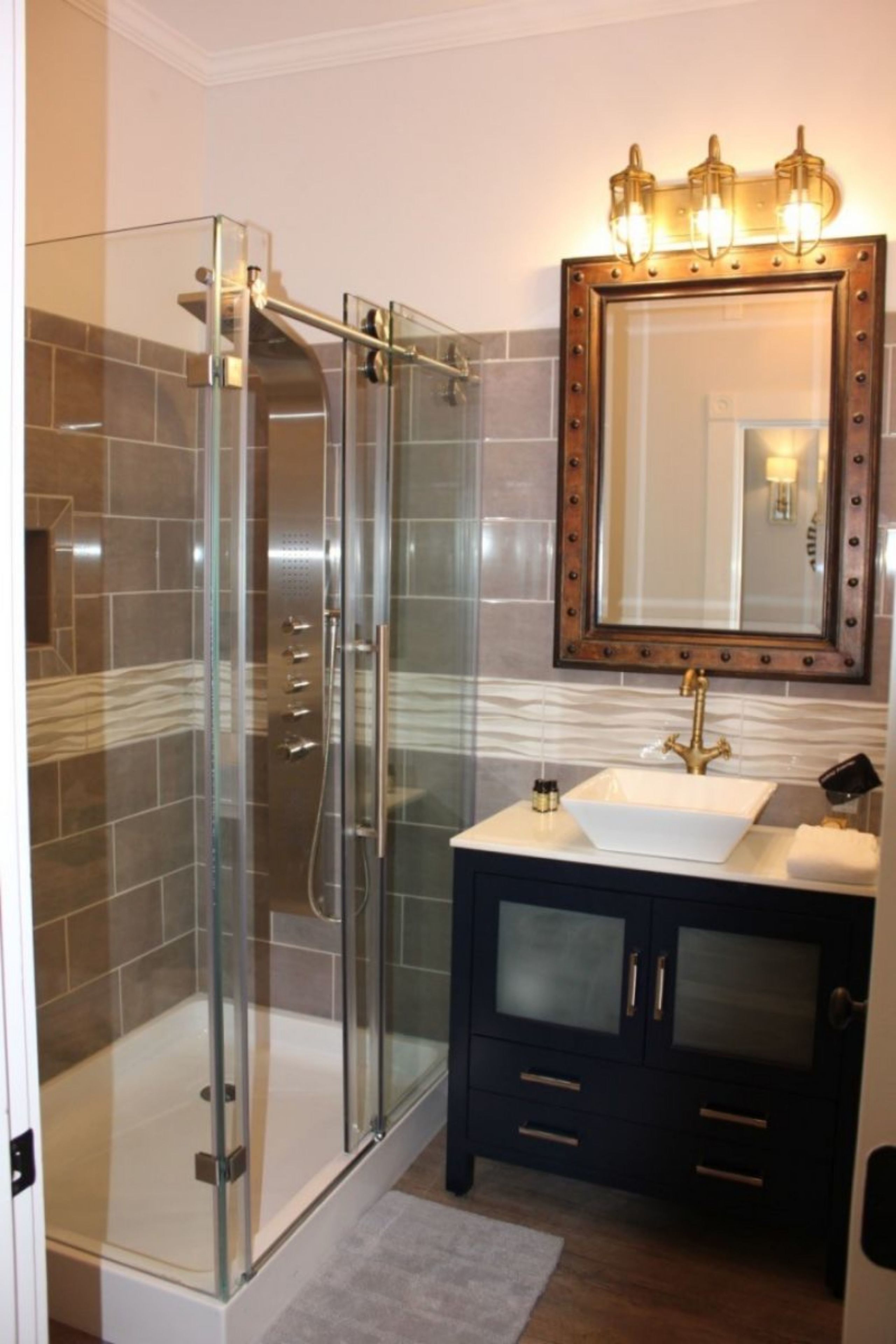 A modern bathroom with a glass-enclosed shower, a vanity with a sink, and a mirror with a decorative frame.