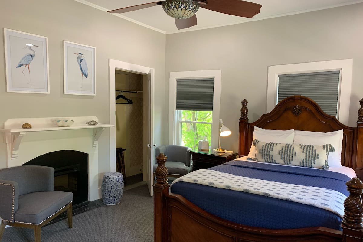 Une chambre à coucher avec un lit en bois, une chaise, un bureau, une cheminée et deux tableaux encadrés accrochés au mur.
