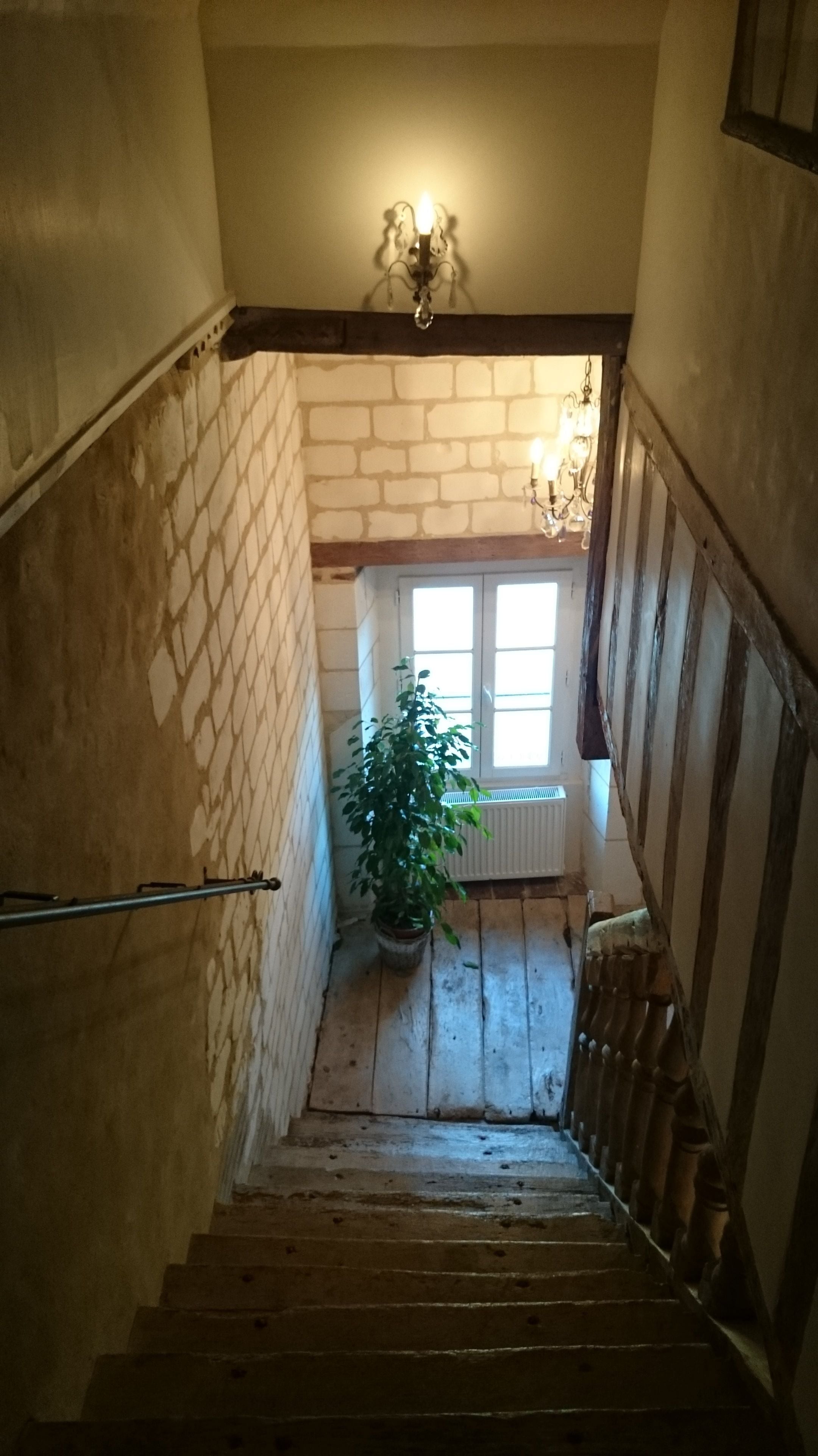 Un escalier en bois avec une rampe, un pot de fleurs et une fenêtre aux montants blancs.