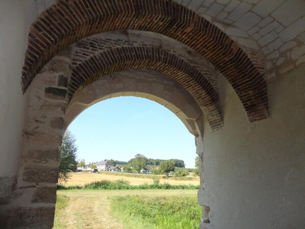 Un arco de piedra conduce a un campo cubierto de césped, con casas al fondo.