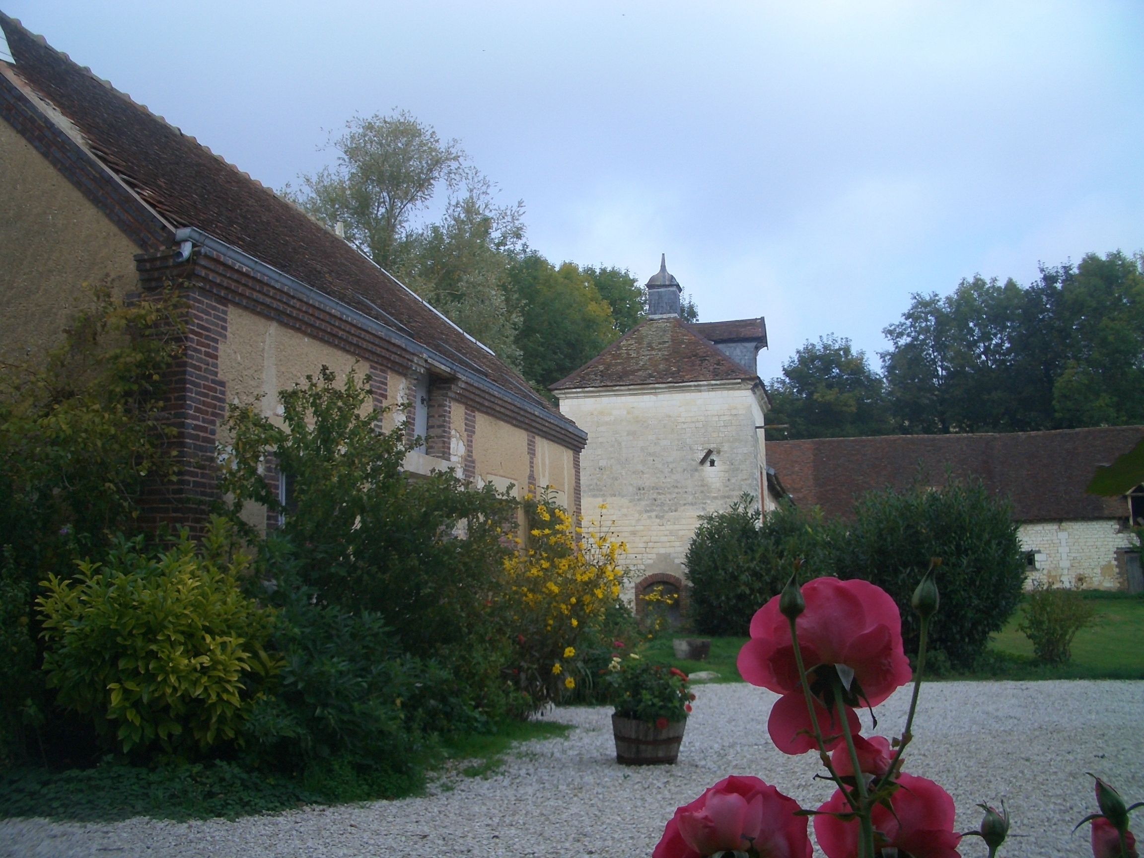 A building with a brick facade and a white wall with a dome. There is a gravel path and greenery around.