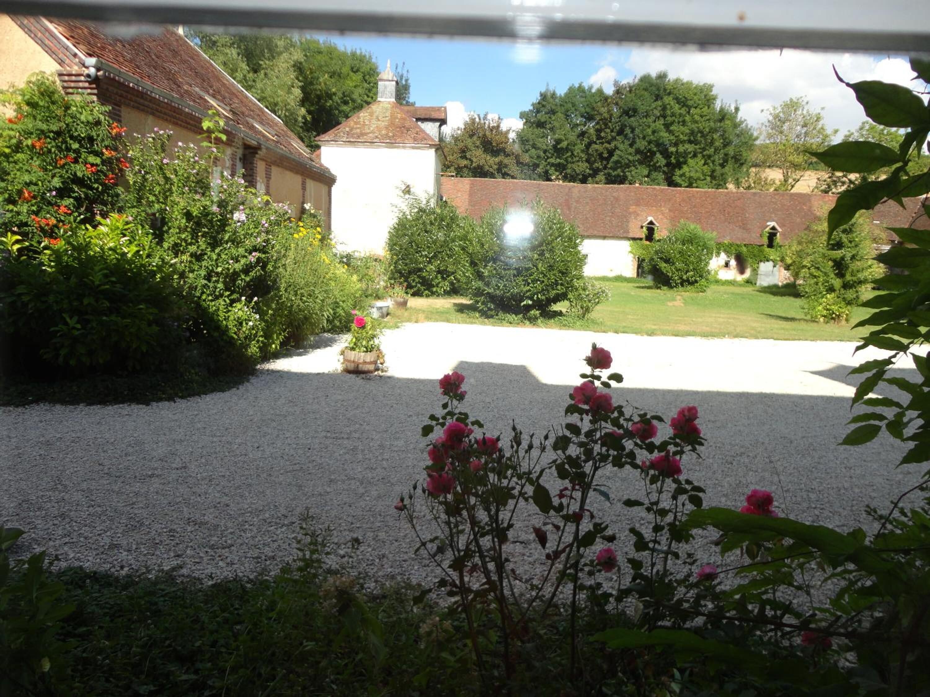 Un jardin avec des allées de gravier, des plantes en fleurs et un bâtiment blanc surmonté d’un toit rouge.