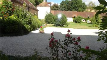 Un jardin avec des allées de gravier, des plantes en fleurs et un bâtiment blanc surmonté d’un toit rouge.