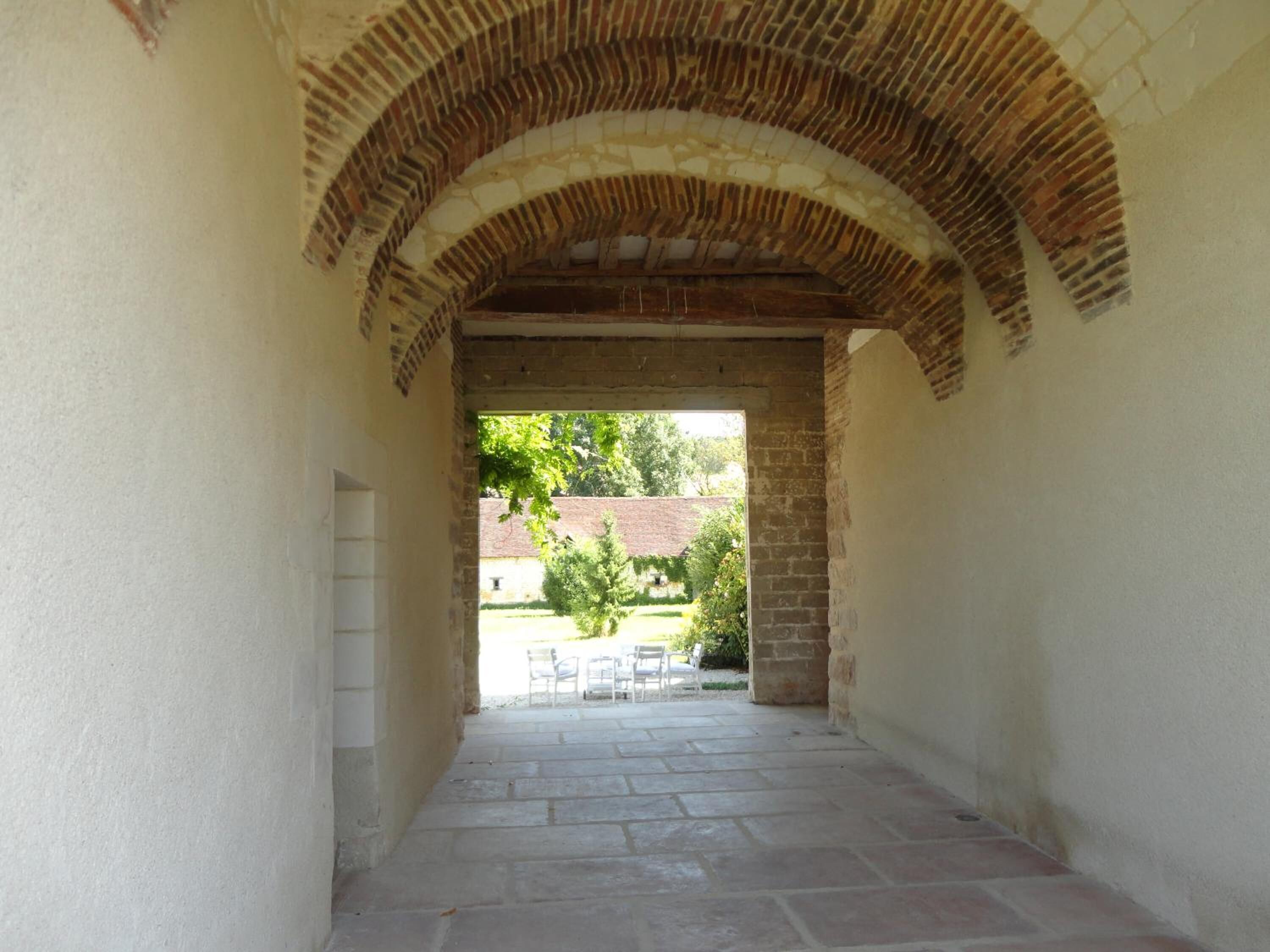 An arched stone corridor with a view of an outdoor seating area.