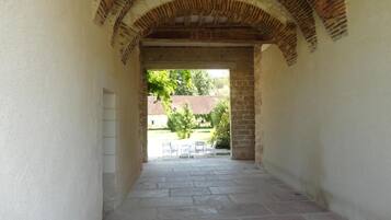 An arched stone corridor with a view of an outdoor seating area.