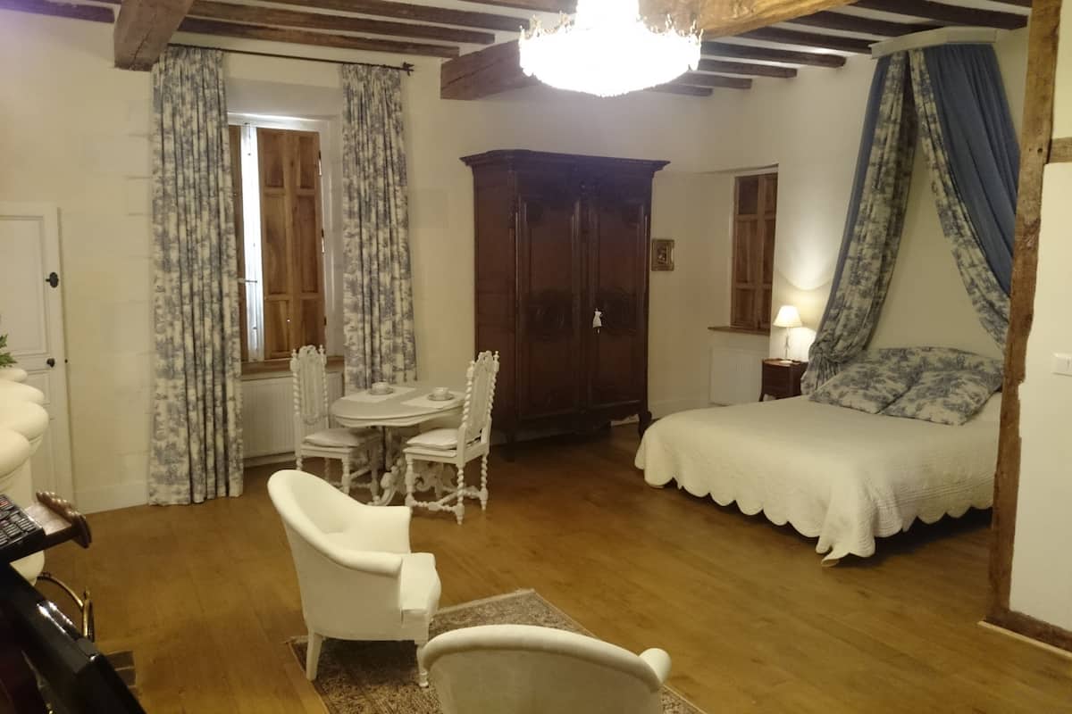 A bedroom with a bed, a wooden wardrobe, a dining table with chairs, and a chandelier.