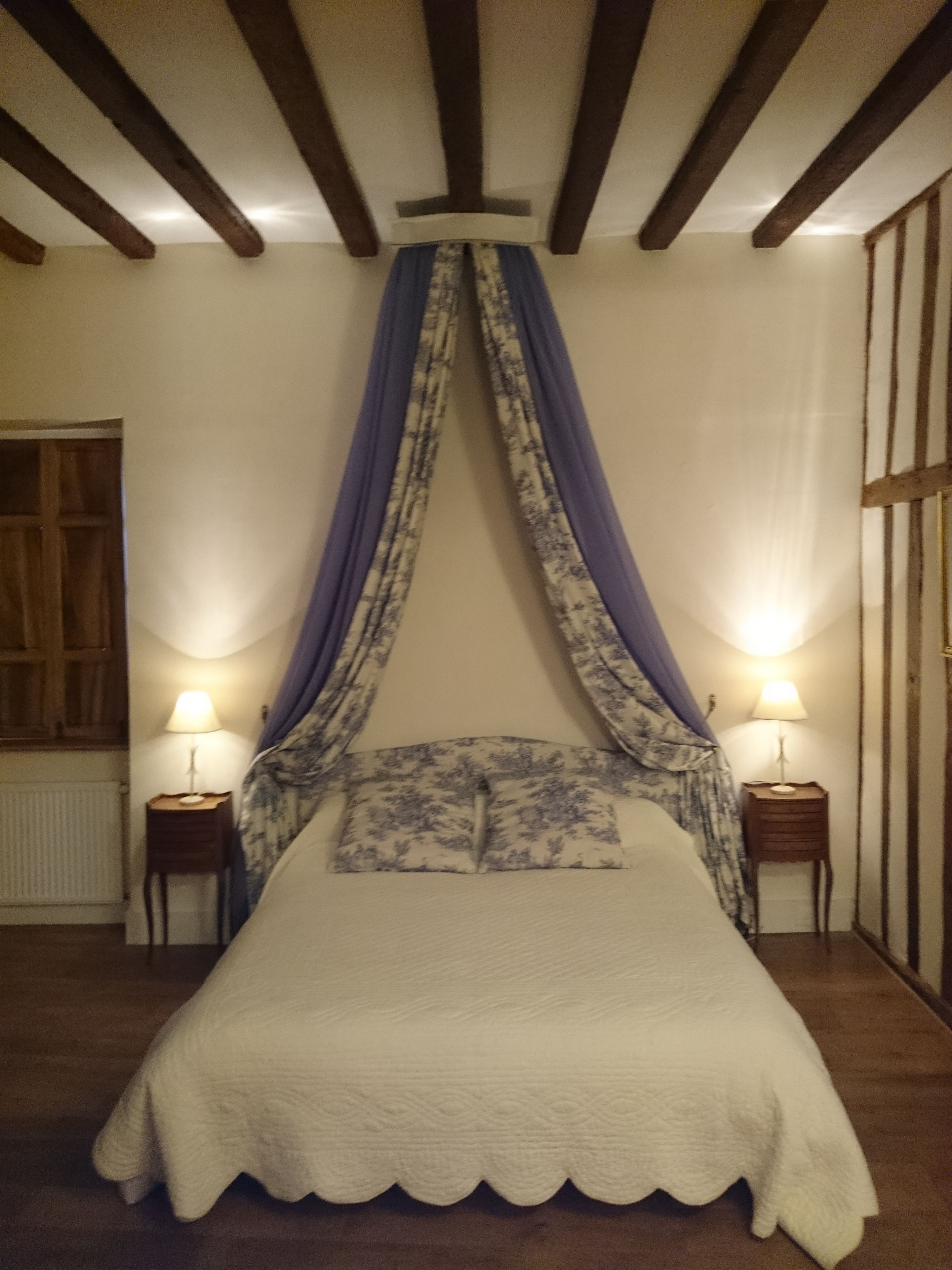 Une chambre à coucher avec un lit à baldaquin, deux tables de chevet avec des lampes, une porte en bois et un radiateur.